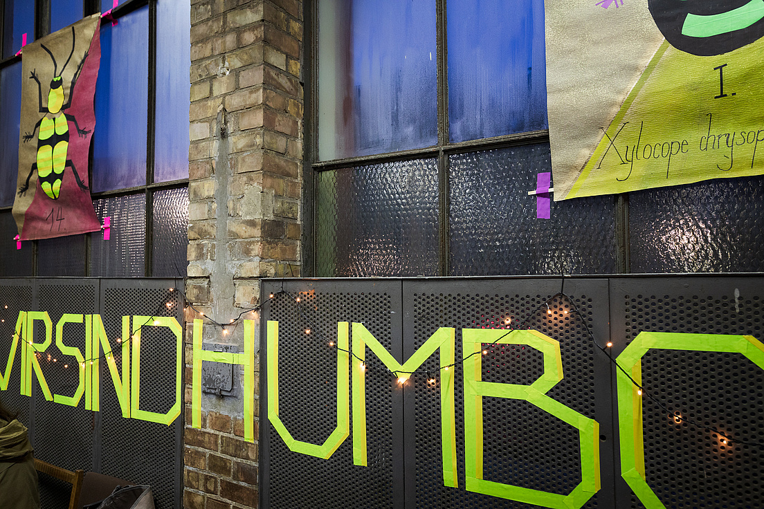 Eine Backsteinwand mit Fenstern. Davor hängen bunte Banner und in gelb aufgeklebten Buchstaben "Wir sind Humboldt"