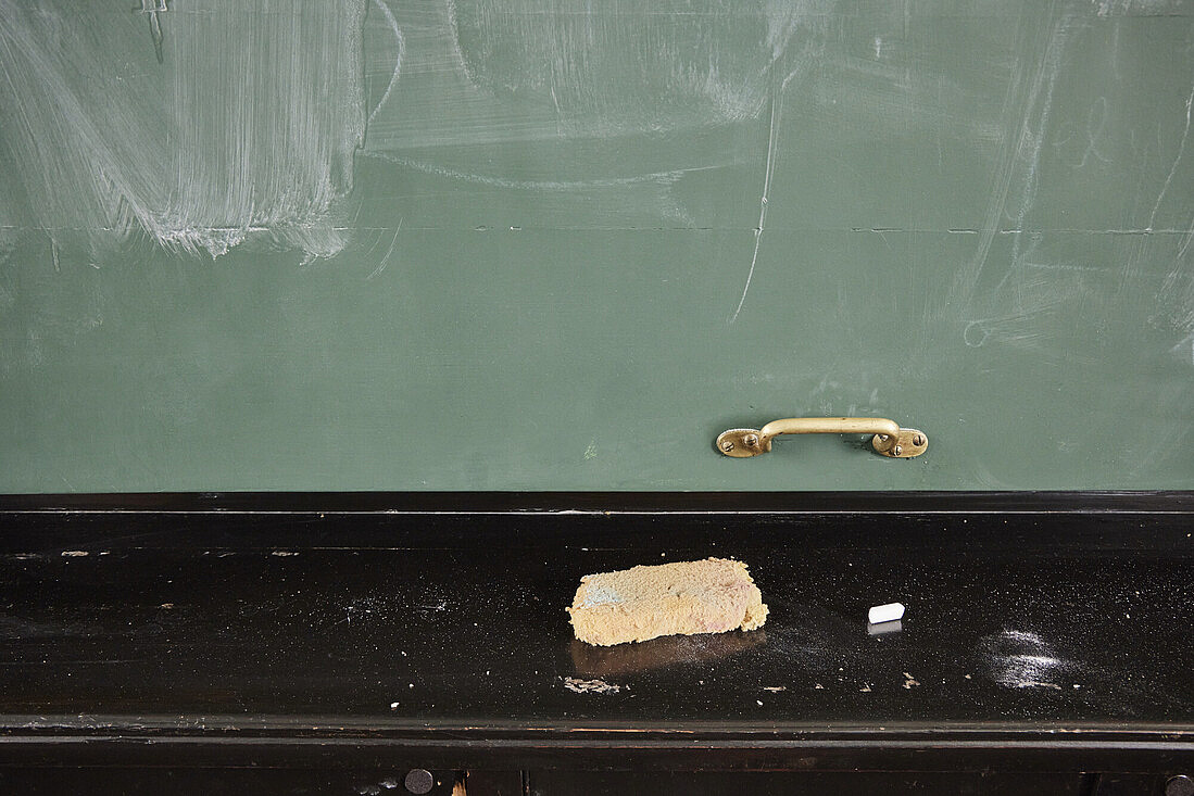 A blackboard with a sponge and the remains of chalk in front of it. The blackboard has been wiped clean, chalk residue is still on it.