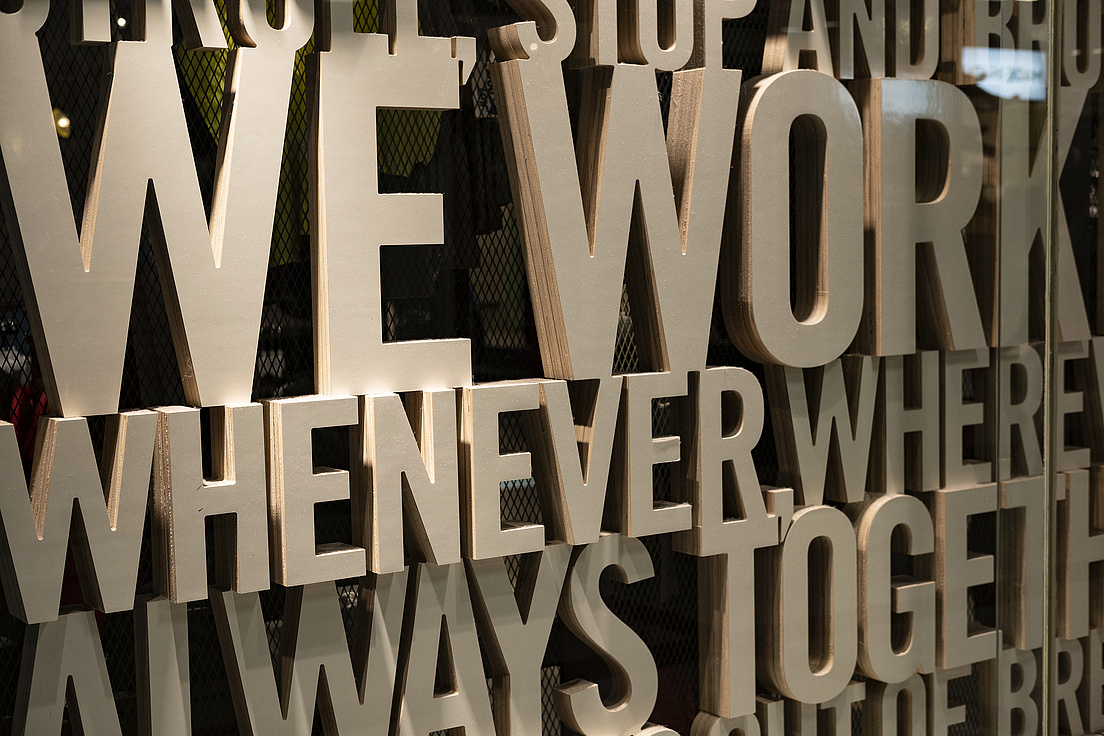 In großen Lettern steht hinter einer Glasscheibe "We Work When We Work Always Together"