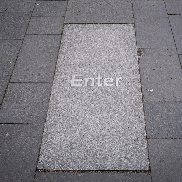 Enter-Bodenplatte Eine hellgraue Bodenplatte auf der Enter steht.