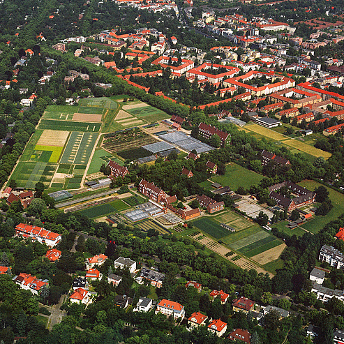 Luftaufnahme Campus Dahlem Eine Luftaufnahme auf den Campus Dahlem. Man sieht zahlreiche Felder, Gewächshäuser und Backsteingebäude.