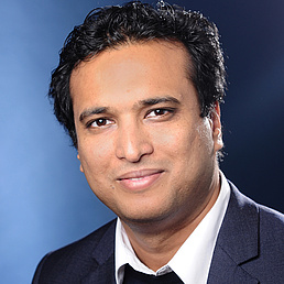 Kallol Ray Kallol Ray hat ein weißes Hemd, einen dunkelfarbenen Pullover und einen schwarzen Anzug an. Er blickt freundlich in die Kamera.