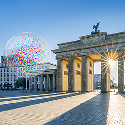 Keyvisual Berlin University Alliance Ein Bild vom Brandenburger Tor, im Hintergrund blauer Himmel und Sonnenstrahlen, die zwischen den Säulen hervorscheinen. Im Bild sind auch vier transparente Blasen mit Konfetti zu sehen.