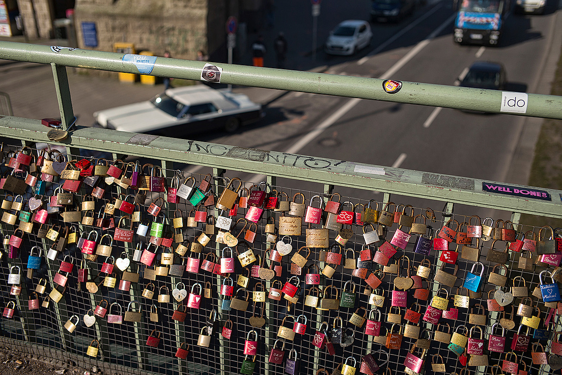 Open-Humboldt-Gesundheit-Bruecke-Inklusion-Matthias-Heyde Das Bild zeigt eine Brücke, deren Geländer mit vielen Schlossern verziert ist. Diese Schlosser sind in verschiedenen Farben und Formen, darunter viele Herzformen, und scheinen von Paaren angebracht worden zu sein, die ihre Liebe symbolisch an der Brücke festigen möchten.