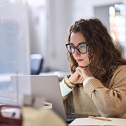 Young professional woman using laptop watching online webinar at work. Young working woman following an online webinar on her laptop at work.
