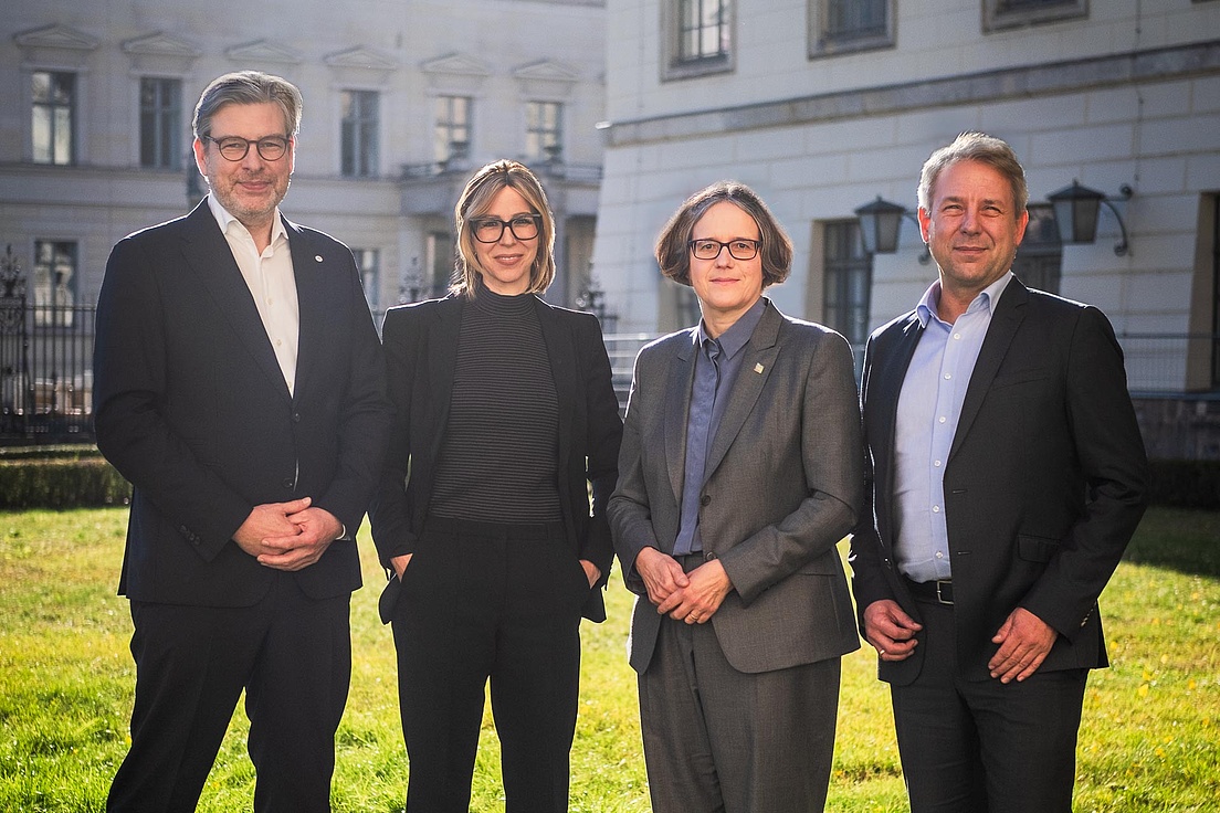 Das Präsidium der Humboldt-Universität zu Berlin Die vier Mitglieder des Präsidiums der HU stehen nebeneinander auf einer Wiese. Im Hintergrund Gebäude der HU.
